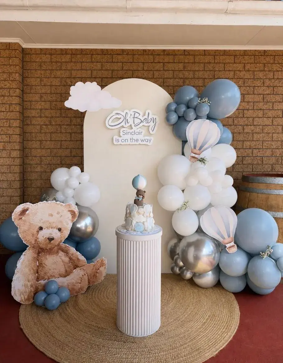 Blue balloon baby shower backdrop with teddy bear, hot-air balloons and cake plinth